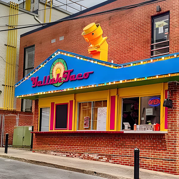 The vibrant Yallah Taco restaurant exterior, featuring a blue awning, yellow walls, and a large sombrero sign.