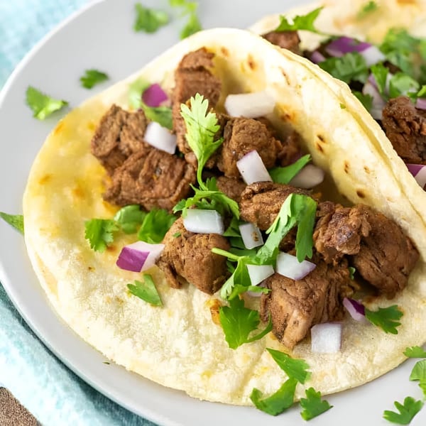 Close-up of two Yallah Taco carne asada tacos with cilantro and diced red onions.