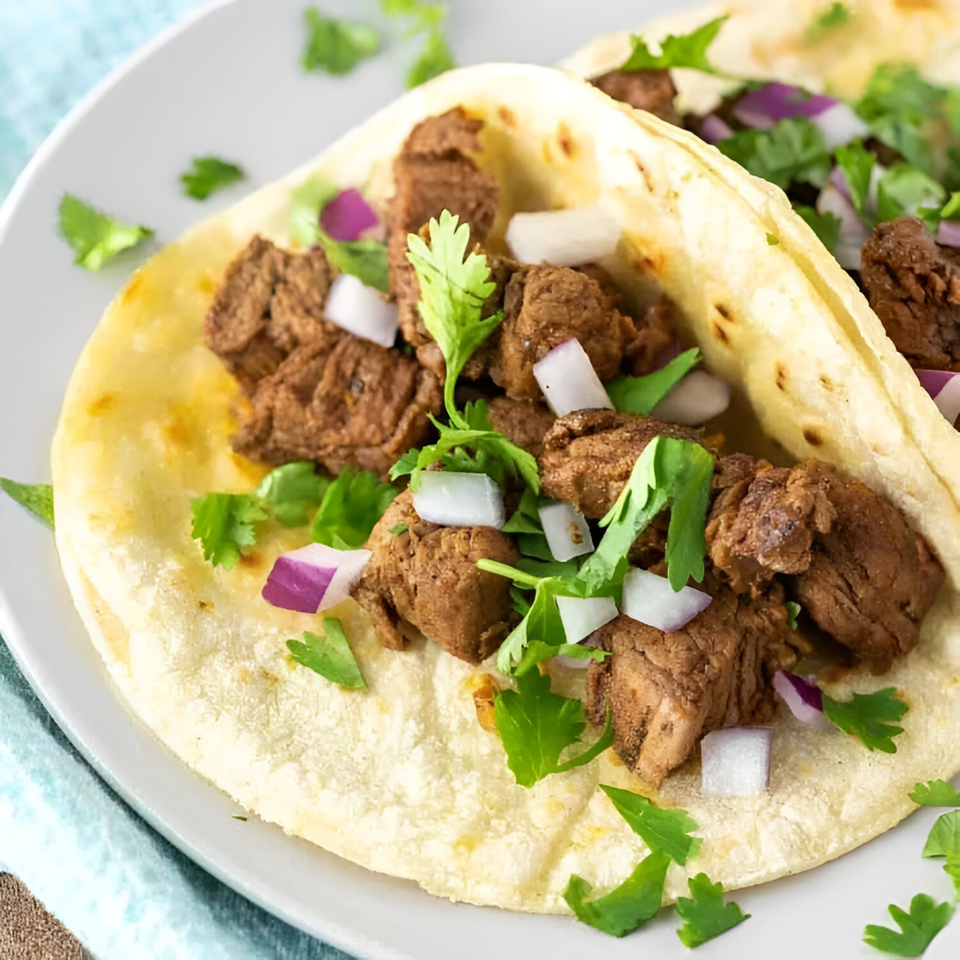 Close-up of two Yallah Taco carne asada tacos with cilantro and diced red onions.