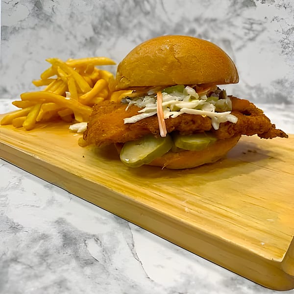 Yallah Taco's fried chicken sandwich with coleslaw and pickles, served with fries on a wooden board.