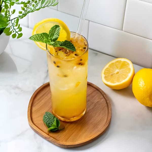 A refreshing passion fruit drink with lemon and mint on a wooden tray, with lemons nearby.