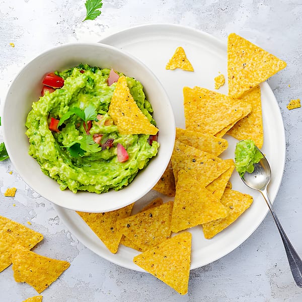 A white bowl of Yallah Taco guacamole with tomatoes and cilantro, surrounded by tortilla chips.