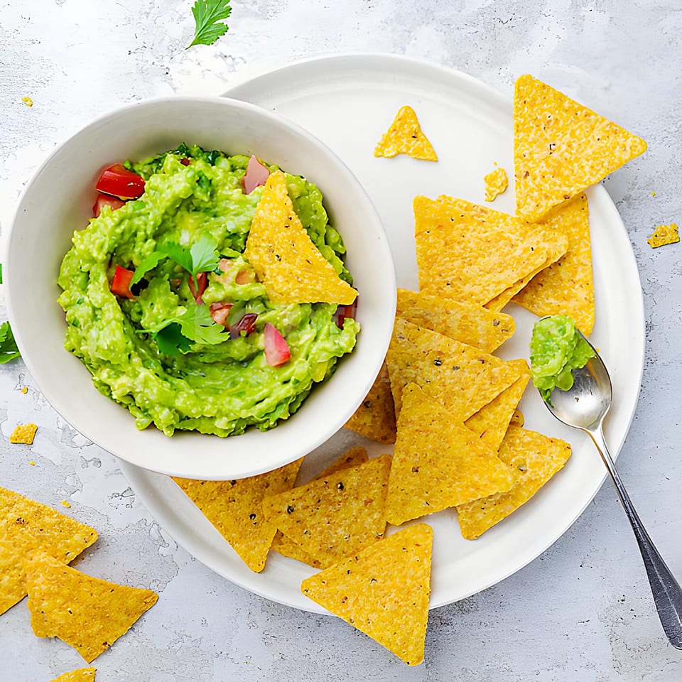 A white bowl of Yallah Taco guacamole with tomatoes and cilantro, surrounded by tortilla chips.