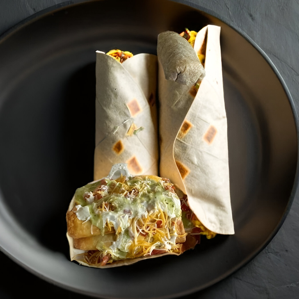 Two Yallah Taco burritos and a loaded burrito bowl with green and white sauce on a dark plate.