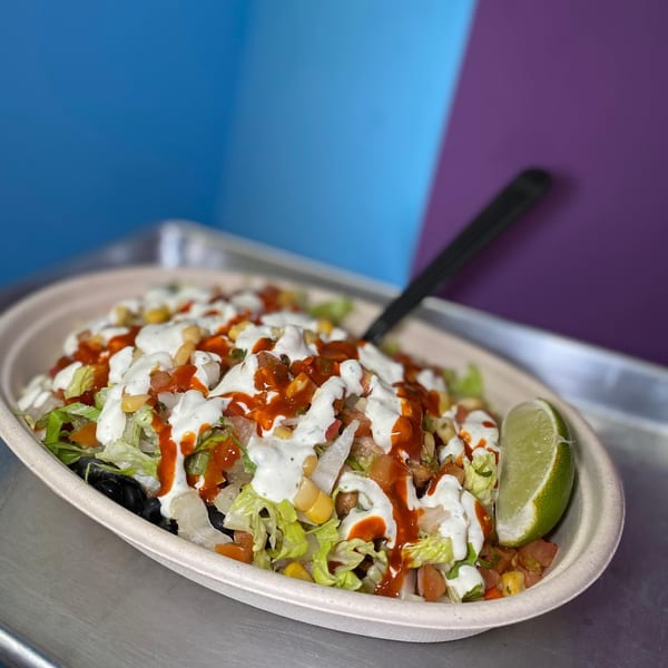 A Yallah Taco salad bowl with lettuce, corn, salsa, and sauces, garnished with a lime wedge.